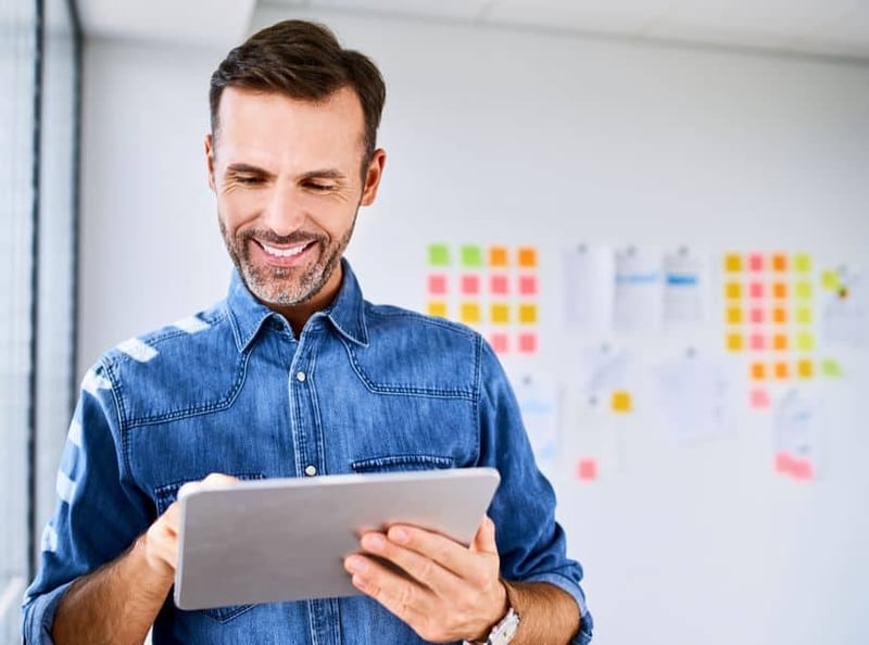 Man in blue denim polo smiling while checking his tablet